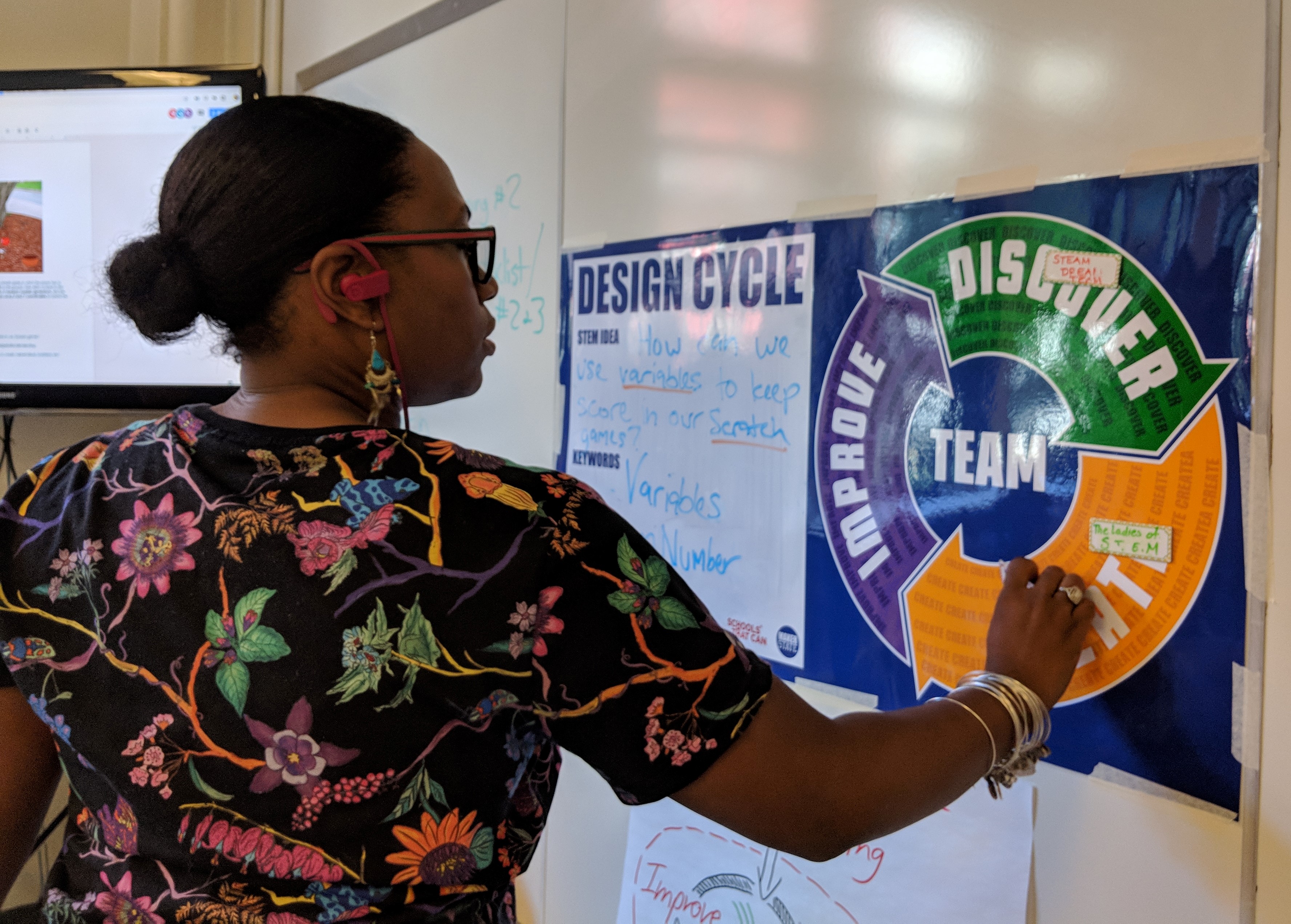 Female teacher with her back to the camera writes on a poster of the MPP Design Cycle.