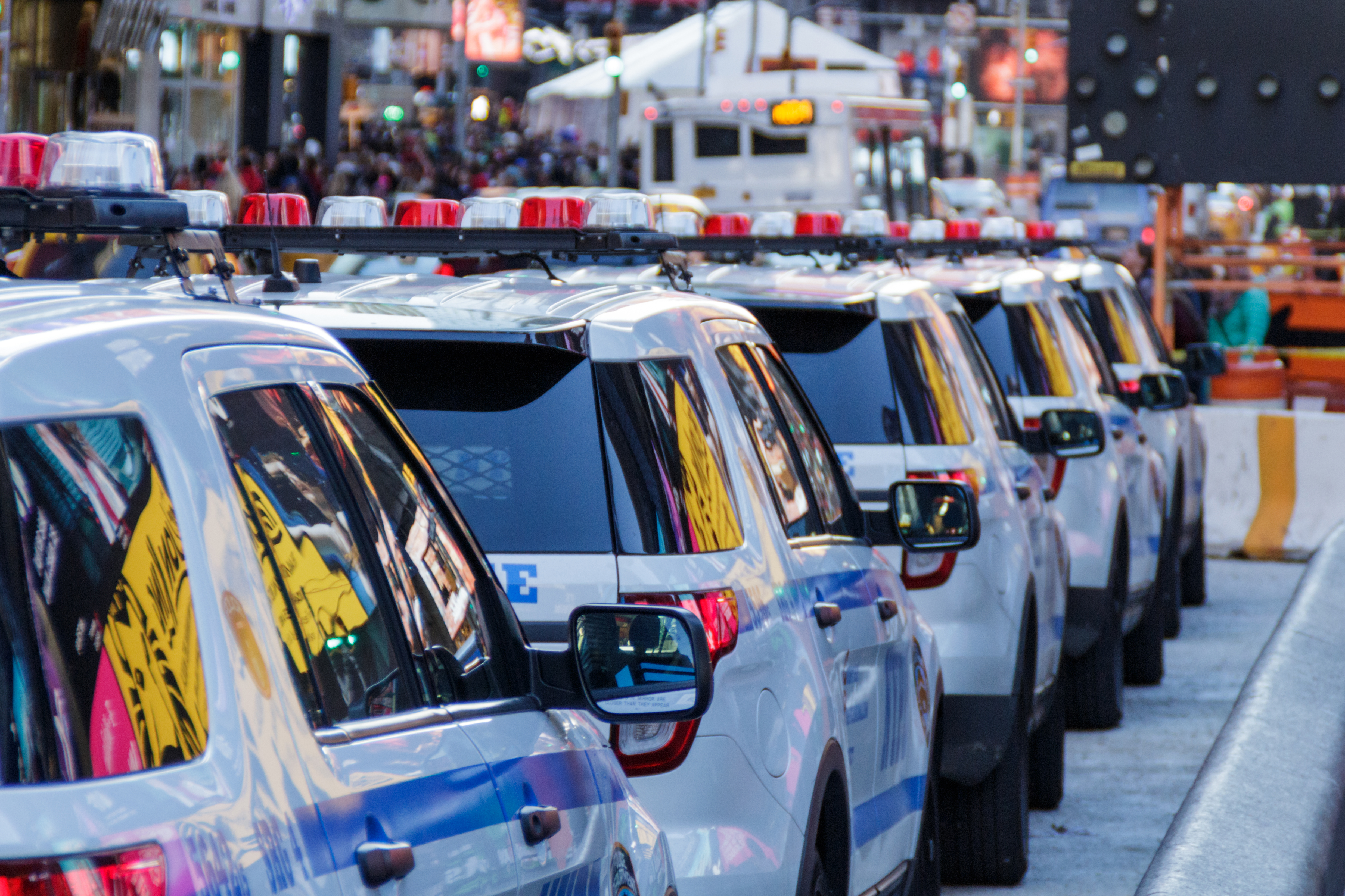Four NYC Police cars are parked along a busy NYC street.