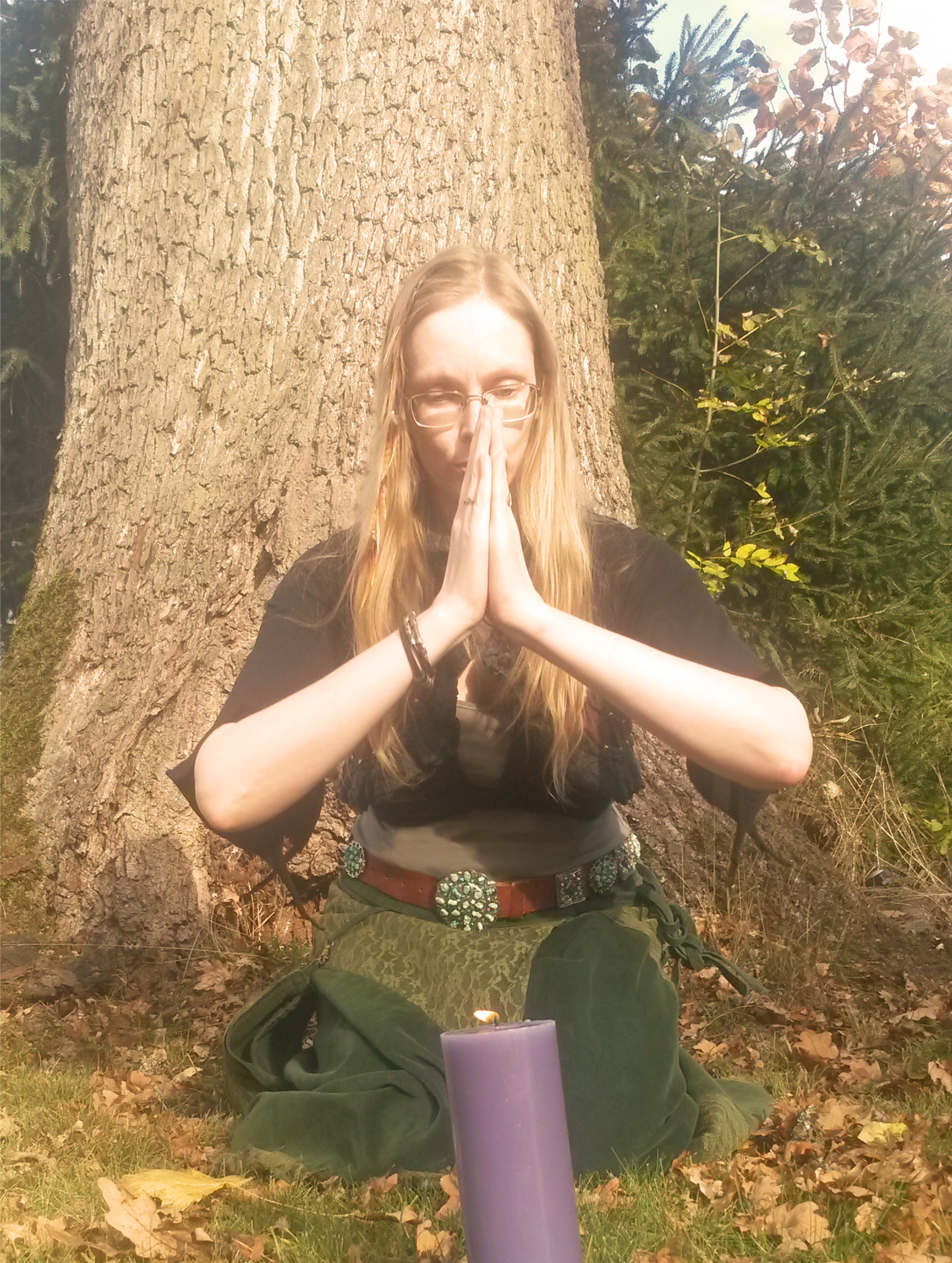 Stefanie Dietrich meditierend vor einer Eiche, lila Kerze im Vordergrund