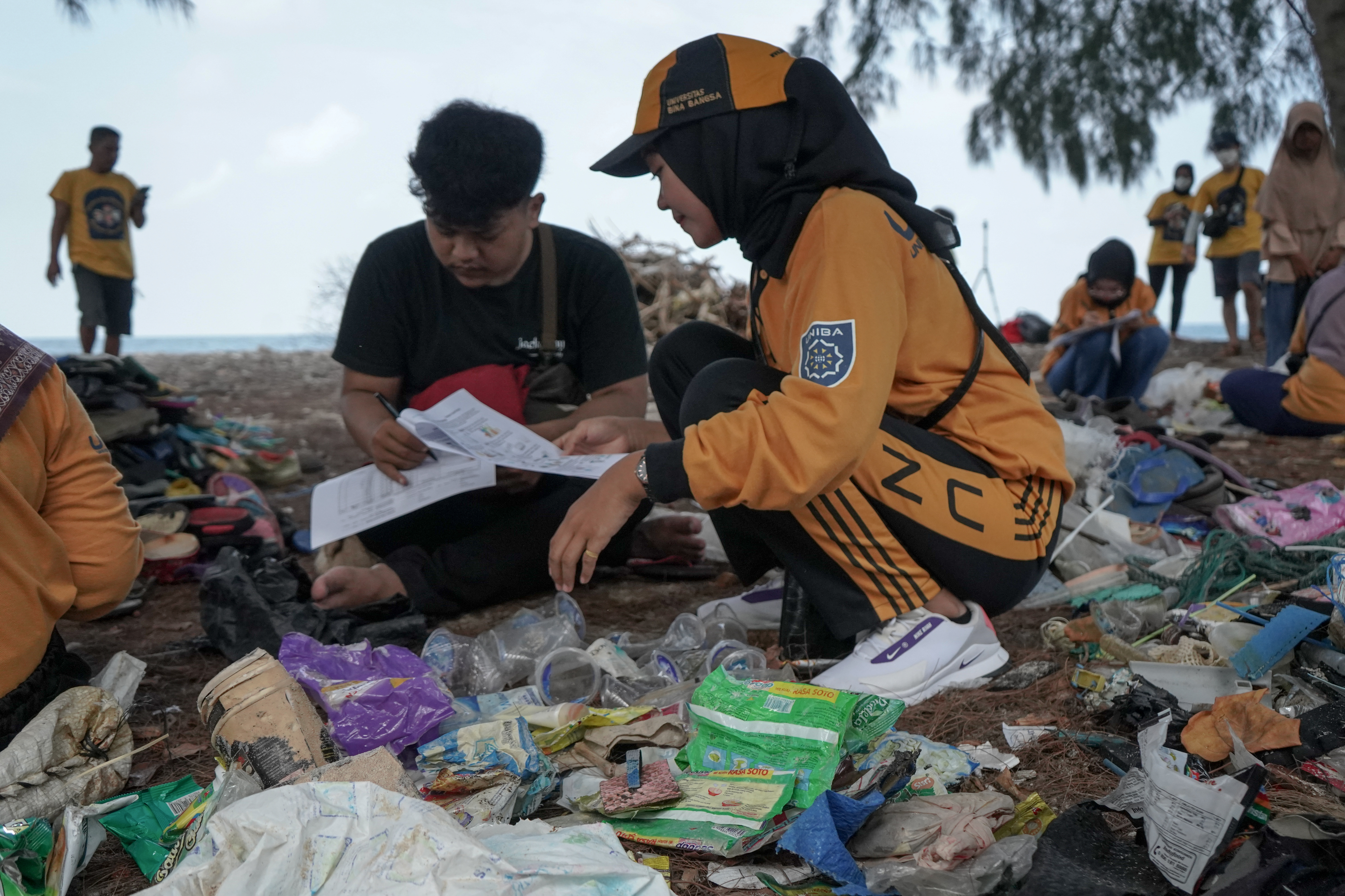 Image taken at the 2022 brand audit in Indonesia with Greenpeace Ocean Defender. A young person in the foreground is pictured holding an identification sheet while another person records data.