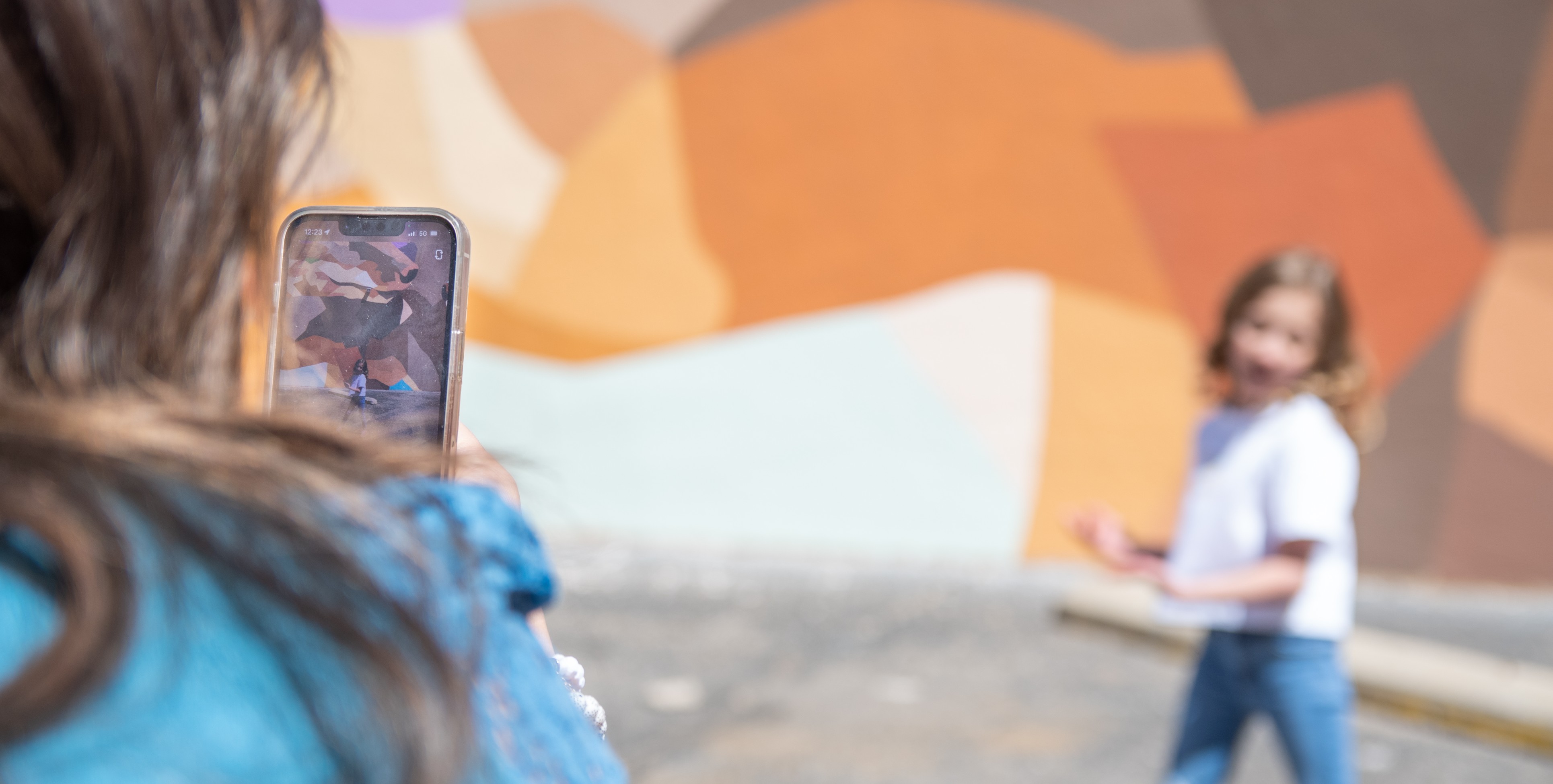 Mother and daughter take photo in front of outdoor mural.